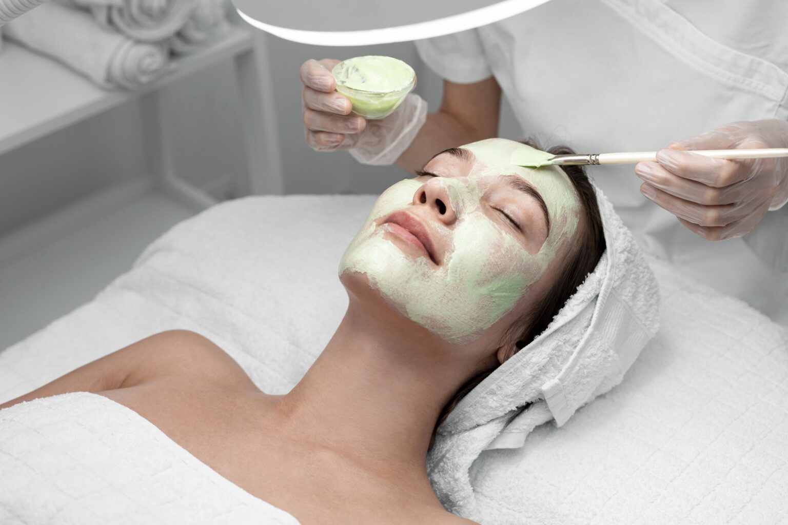 Esthetician applying a chemical peel to a client’s face in a clinical setting.