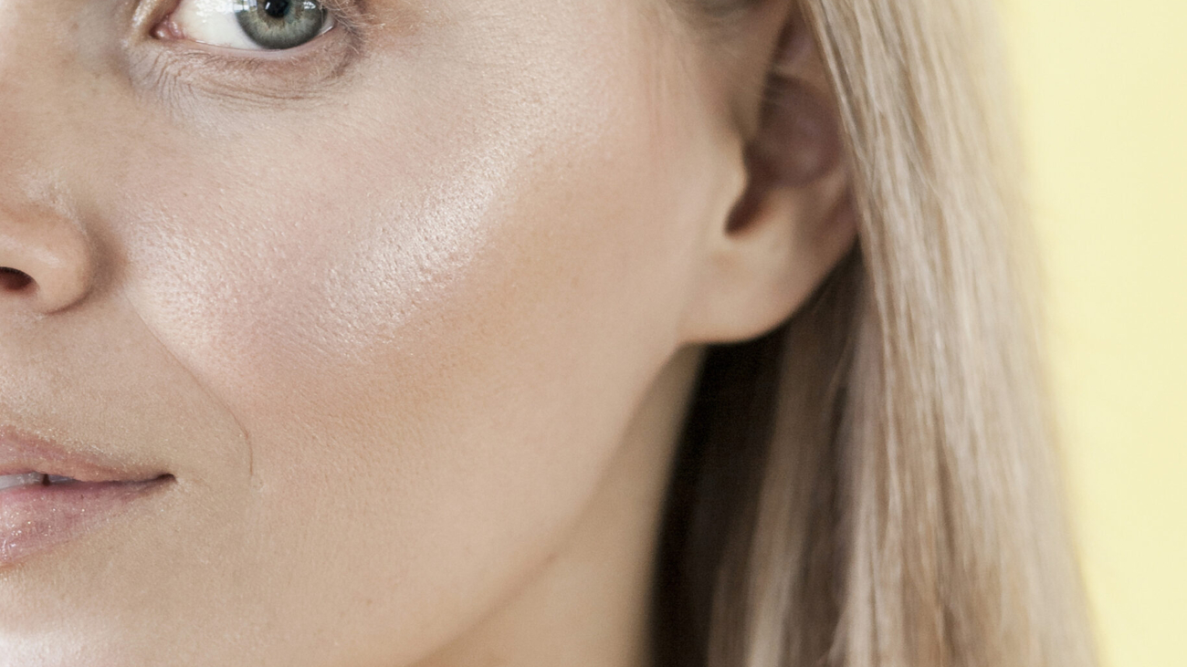 Woman with radiant, dewy skin smiling in natural sunlight.