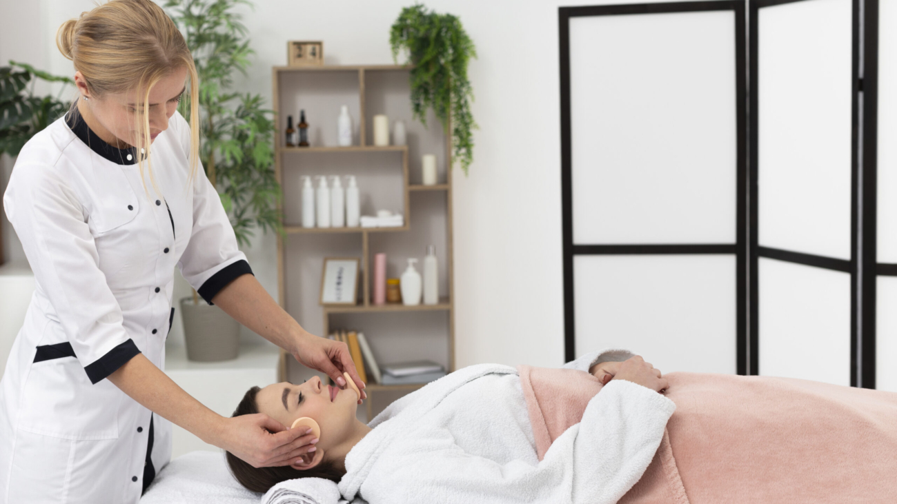 Aesthetician applying facial treatment to a relaxed woman in a spa setting.